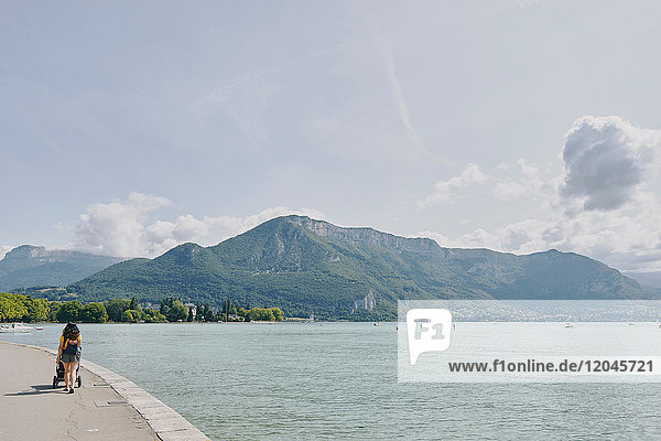 Rear view of woman strolling with pushchair waterfront at Lake Annecy  Annecy  Auvergne-Rhone-Alpes  France