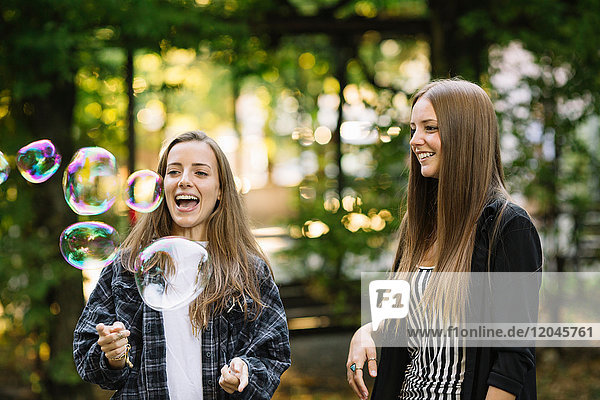Zwei junge Freundinnen  die im Park Blasen platzen lassen