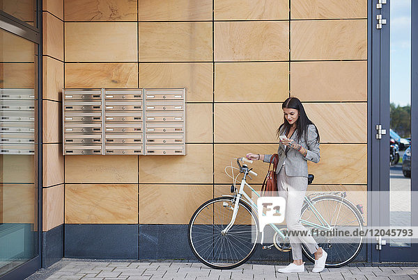 Geschäftsfrau neben Bürogebäude  Fahrrad fahren  Smartphone benutzen
