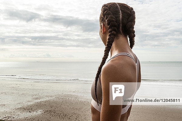 Junge weibliche Läuferin mit Haarzöpfen  die vom Strand aufs Meer blickt