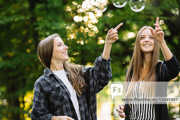 Zwei junge Freundinnen  die im Park Blasen platzen lassen