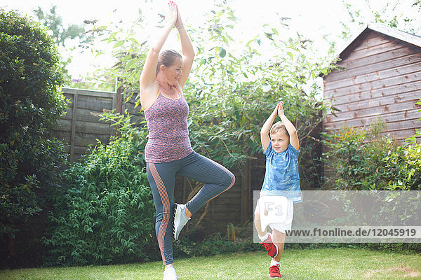 Mutter und Sohn üben im Garten  stehend in Yogastellung