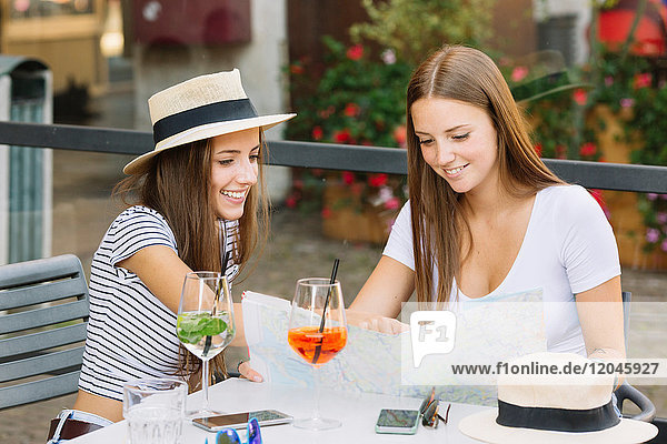 Zwei junge Freundinnen schauen im Straßencafé auf die Karte