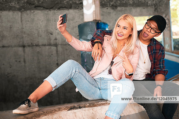 Junges Skateboard-Paar sitzt auf der Rampe und nimmt Smartphone-Selfie