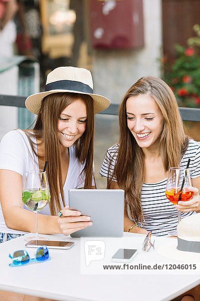 Zwei junge Freundinnen schauen sich im Straßencafé ein digitales Tablet an