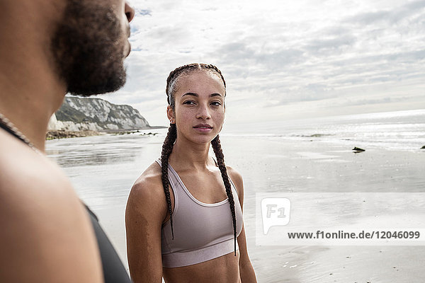 Young male and female runners gazing at each other on beach