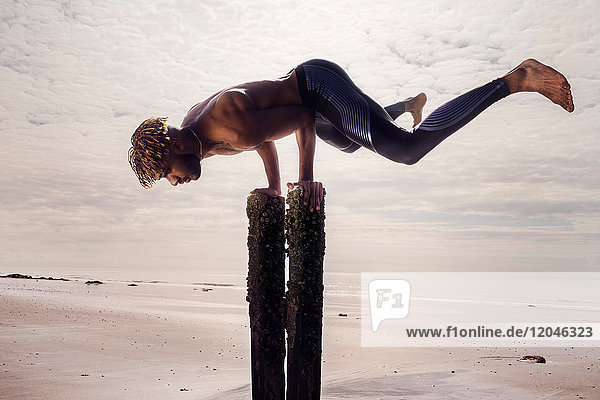 Junger Mann trainiert  macht Handstand an hölzernen Strandpfosten