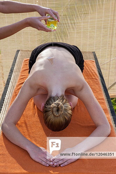Frau in Wellness-Umgebung  die sich zur Vorbereitung auf eine Massage Öl auf den Rücken gießen lässt