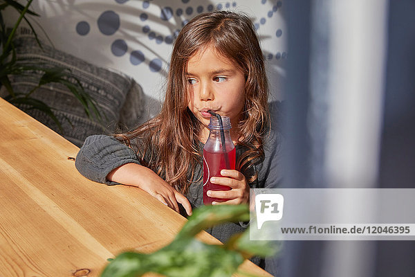 Young girl sitting at table  drinking juice from bottle using straw