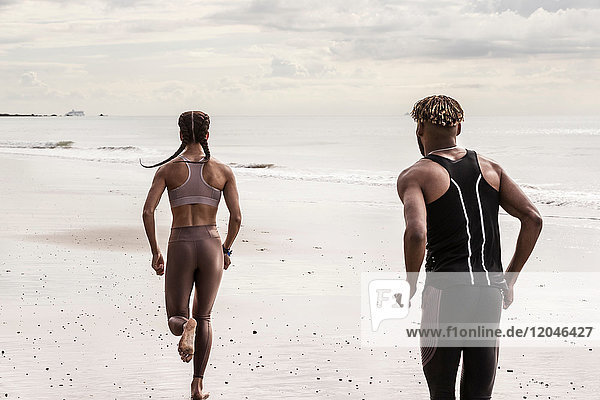 Rear view of young male and female runners running on beach