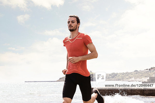 Junger männlicher Läufer läuft am Strand entlang