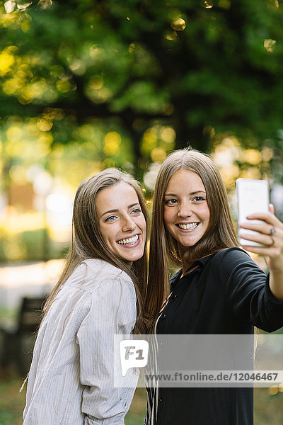 Two young female friends posing for smartphone selfie in park
