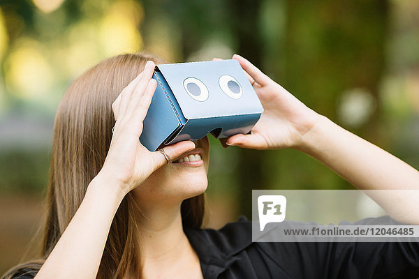 Young woman looking up through cardboard binoculars in park