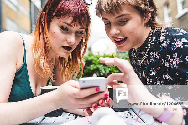 Two young women at sidewalk cafe table looking at smartphone