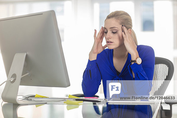 Junge Büroangestellte sieht gestresst auf Schreibtisch