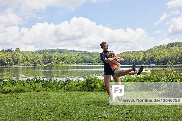 Girl swinging young girl around on grass  beside lake
