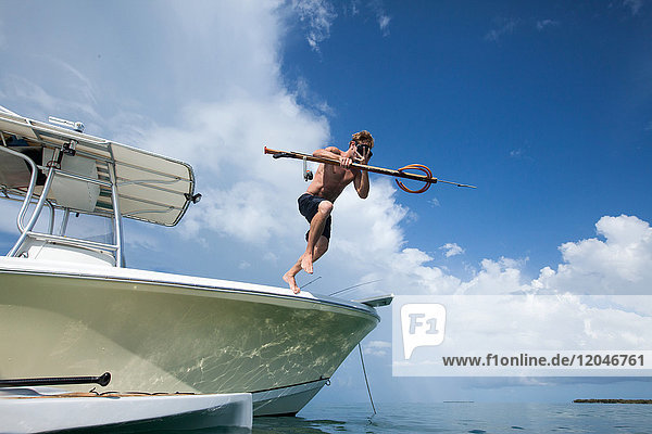 Mann  der vom Boot ins Wasser springt und einen Fischerspeer trägt