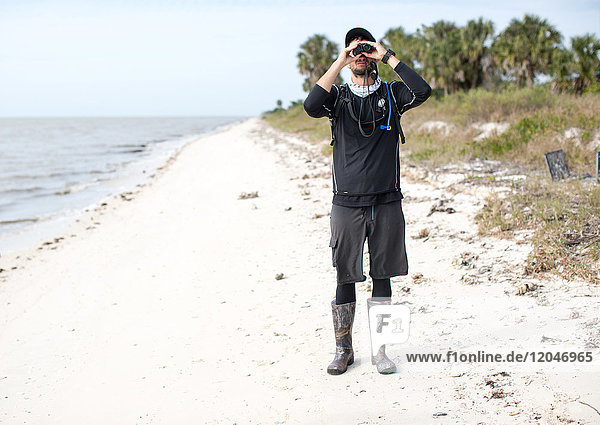 Man standing on beach  looking through binoculars  front view