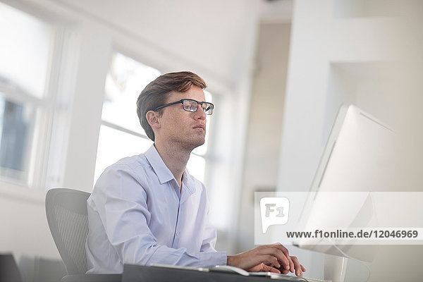 Young male office worker typing at desktop computer