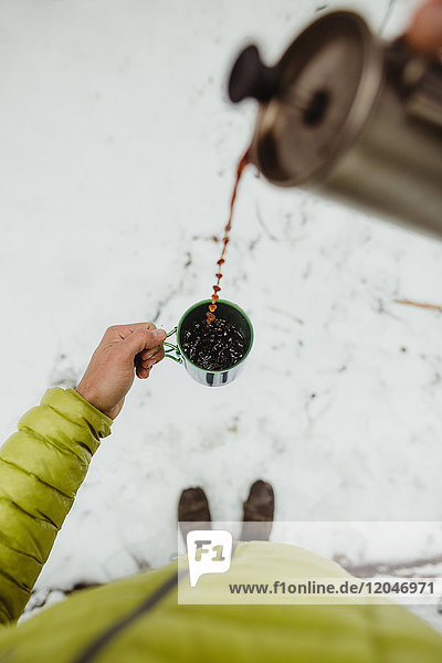 Persönliche perspektivische Ansicht eines männlichen Wanderers  der im Schnee Kaffee aus der Flasche gießt