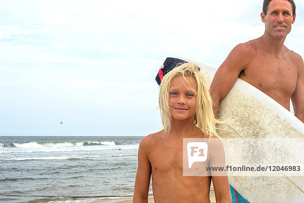 Portrait of mature male surfer and blond haired son on beach  Asbury Park  New Jersey  USA