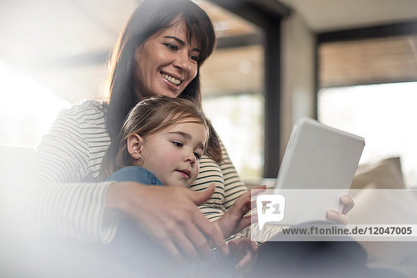 Frau mit Tochter auf Sofa schaut auf digitales Tablet