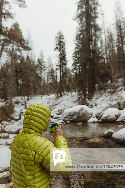 Männlicher Wanderer beim Kaffeetrinken am Fluss im verschneiten Sequoia-Nationalpark  Kalifornien  USA
