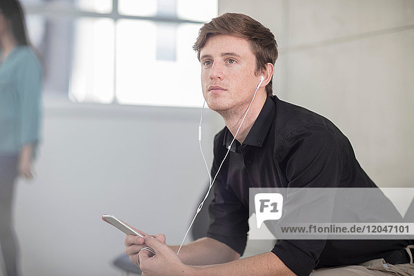 Junger männlicher Büroangestellter träumt am Schreibtisch und hört Kopfhörer