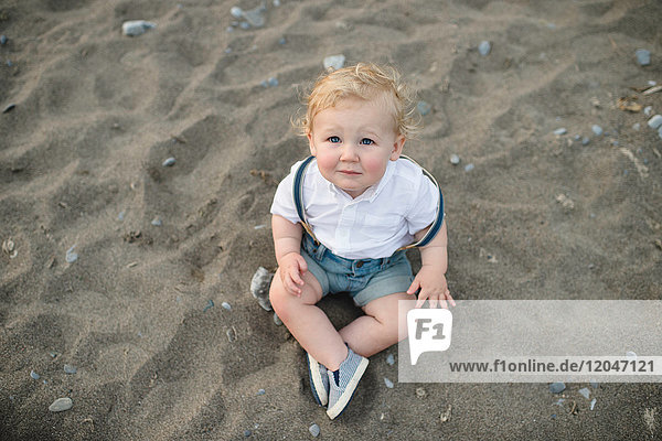 Überkopfporträt eines männlichen Kleinkindes auf Sand sitzend