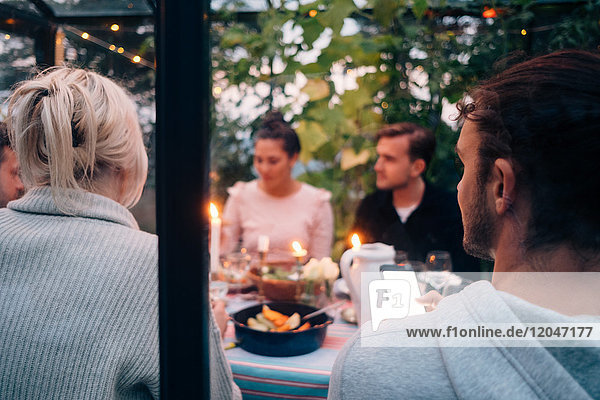 Young male and female friends having dinner party in glass cabin