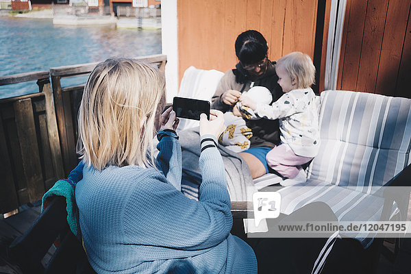 Freund fotografiert Frau beim Spielen mit Kindern über Smartphone in der Ferienvilla