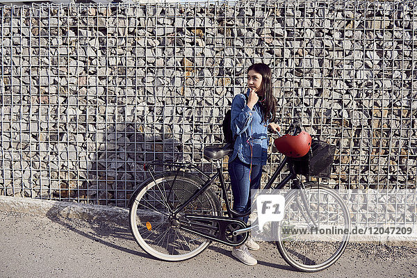 Volle Länge der Frau  die im Stehen mit dem Fahrrad gegen die Steinmauer schaut.