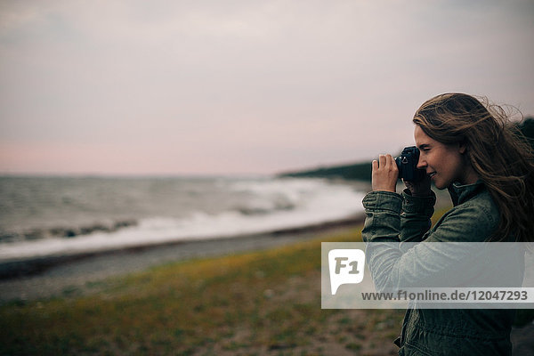 Seitenansicht der jungen Frau beim Fotografieren des Meeres am Strand