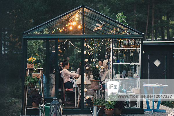 Young multi-ethnic friends enjoying dinner party in glass conservatory room at back yard
