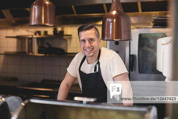 Portrait of smiling young waiter wearing apron in restaurant