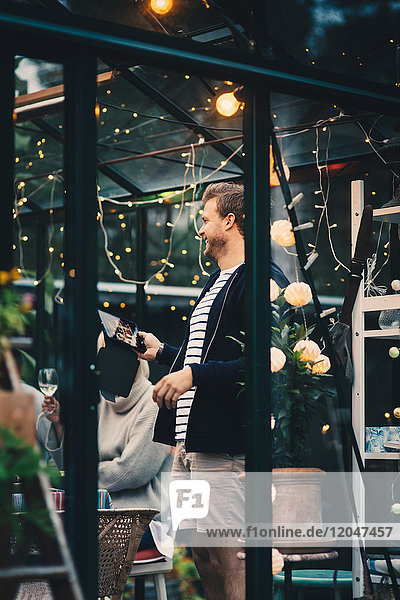 Smiling young man standing with digital tablet by woman at dining table during garden dinner party