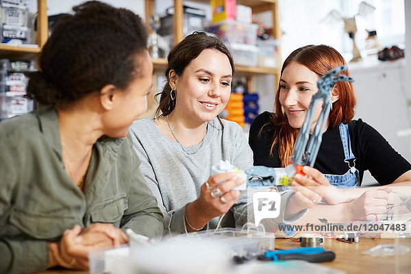 Smiling female inventors sitting with robot model at table in workshop
