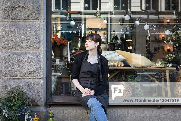 Young female owner sitting with legs crossed on store window sill