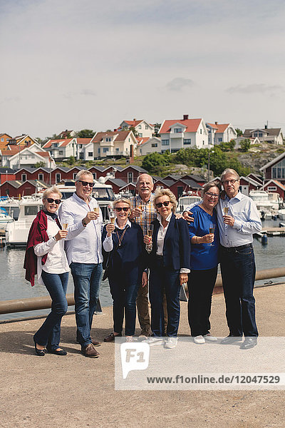Ganzflächiges Porträt von glücklichen Senioren mit Champagnerflöten am Pier während des Urlaubs