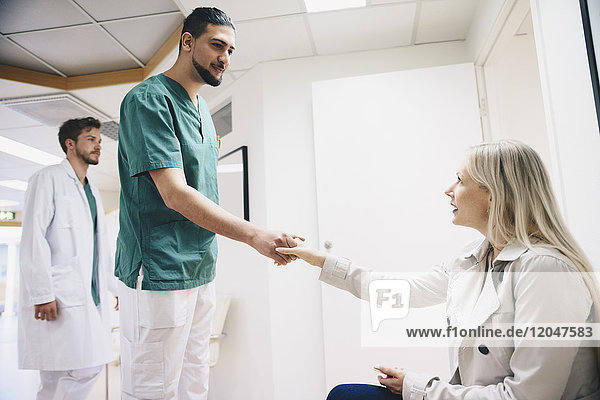 Side view of female patient shaking hands with young male nurse in hospital