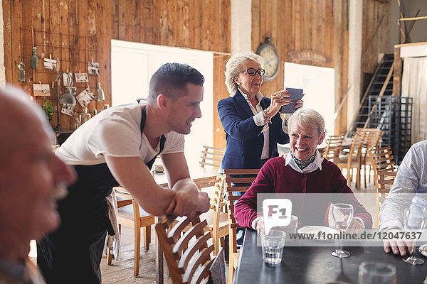Junger Kellner  der sich auf den Stuhl lehnt  während sich ältere Freunde im Restaurant treffen.