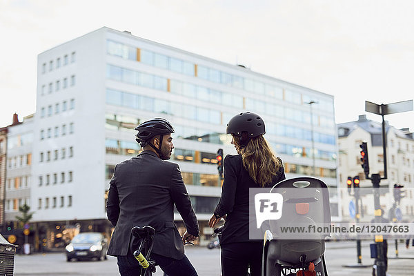 Rear view of business coworkers with bicycles on street in city
