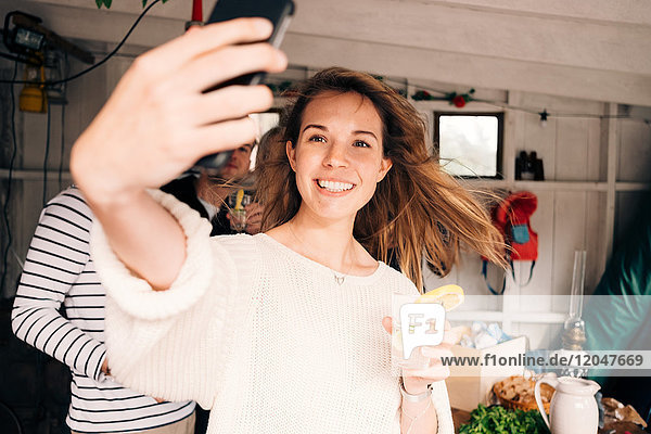 Junge Frau nimmt Selfie auf Smartphone mit Freunden in der Hütte