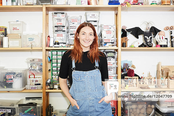 Porträt einer selbstbewussten rothaarigen Technikerin am Regal in der Werkstatt