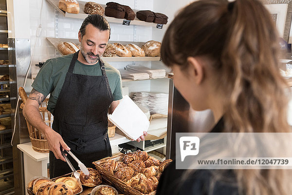 Lächelnder,  reifer,  männlicher Besitzer serviert der Kundin in der Bäckerei frisches Brot.