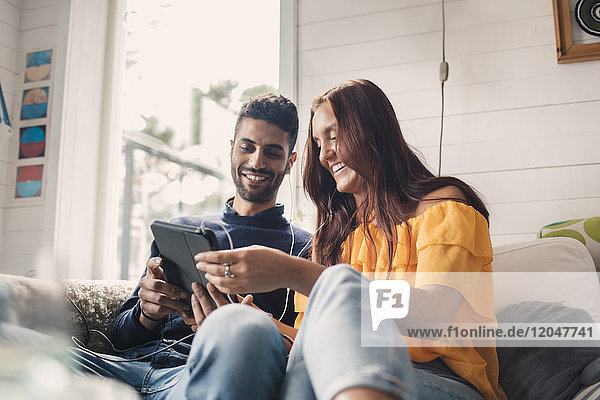 Niedriger Blickwinkel auf glückliche junge Freunde  die sich ein digitales Tablett teilen  während sie zu Hause auf dem Sofa sitzen.
