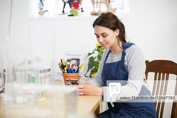 Junge Ingenieurin mit Smartphone am Tisch in der Werkstatt