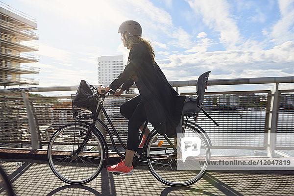 Seitenansicht der reifen Frau beim Radfahren auf der Fußgängerbrücke gegen den Himmel