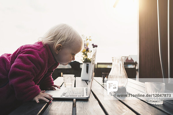 Seitenansicht des Mädchens mit Blick auf den Laptop auf dem Tisch in der Ferienvilla gegen den klaren Himmel