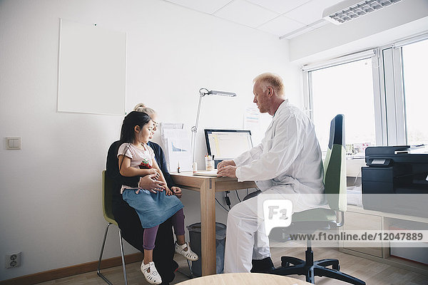 Mature doctor sitting with woman and girl in office at hospital